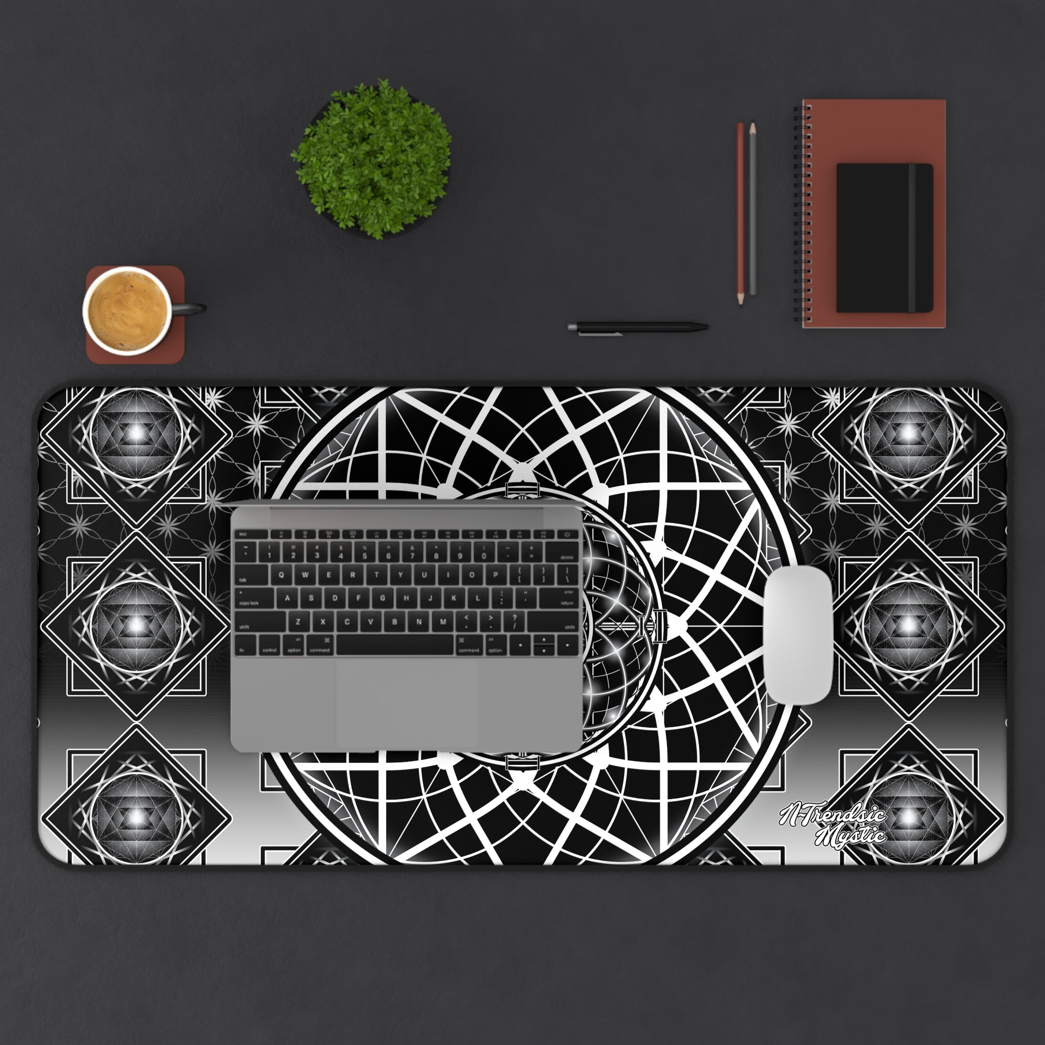 Desk setup with a geometric design mouse pad, laptop, mug, pen, and notebook on a dark surface.