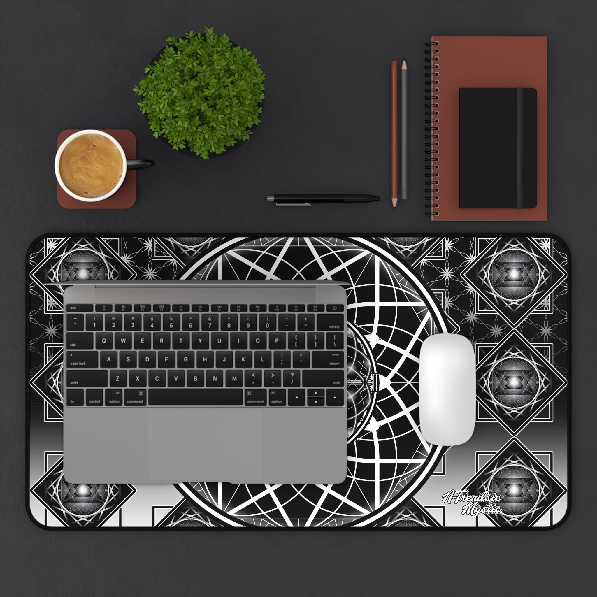 Desk setup with a laptop, mouse, and stationery items on a black surface with a geometric patterned mat.