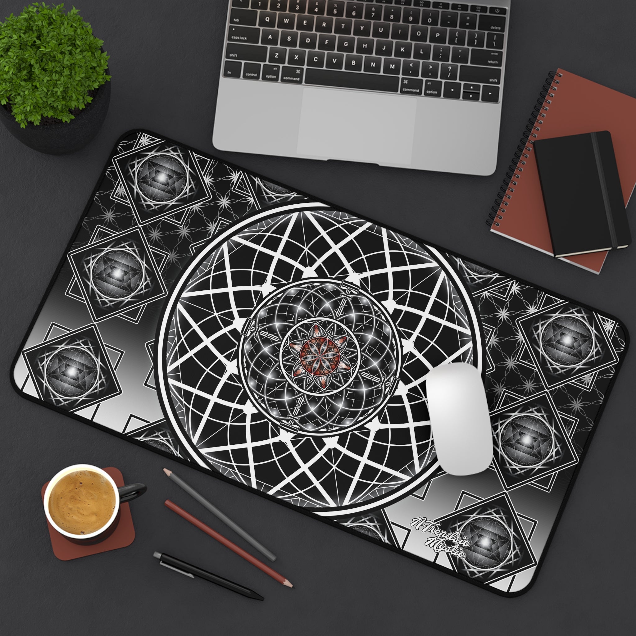 Desk setup with a geometric design mouse pad, laptop, notebook, and coffee cup.