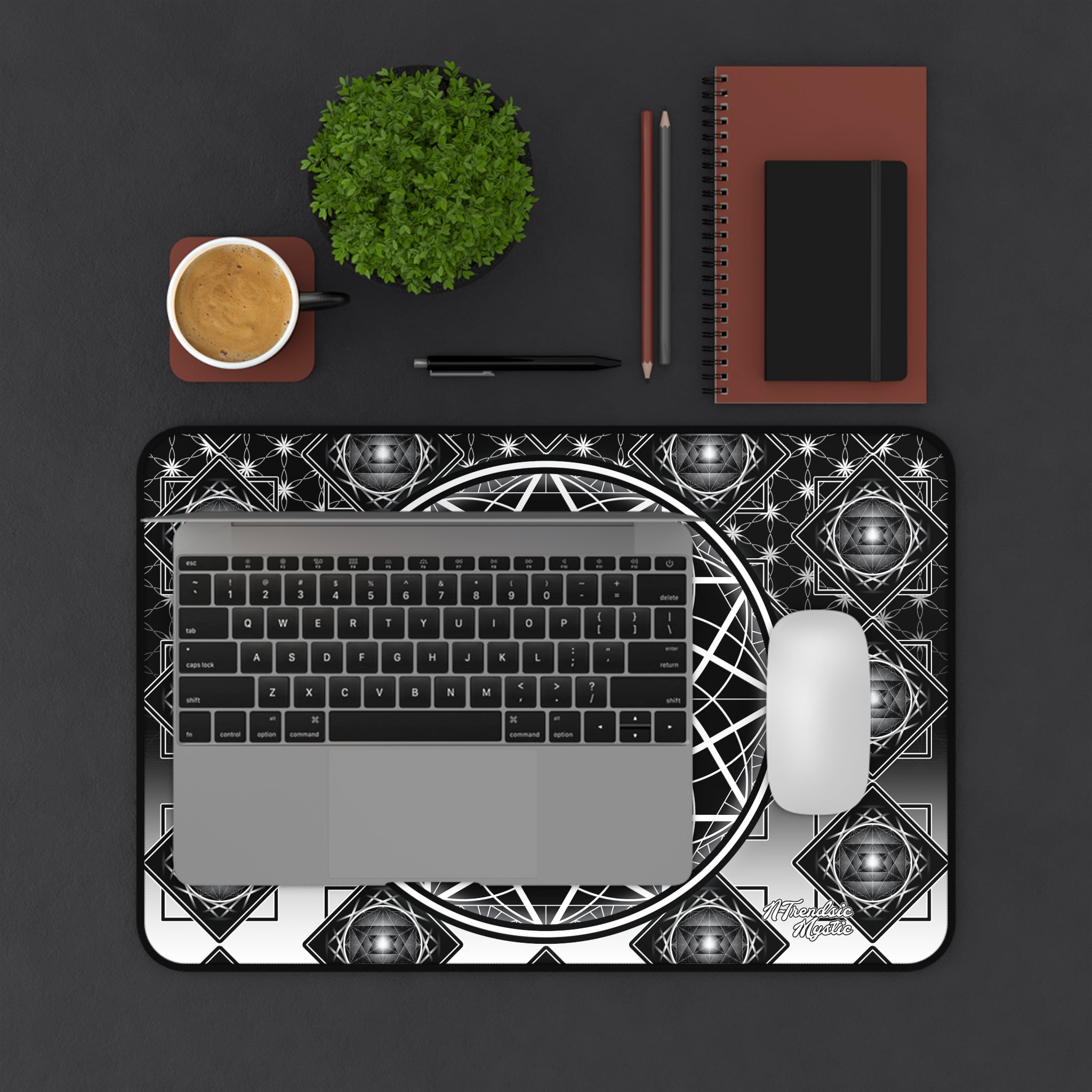Laptop on a decorative black and white mat with a cup, plant, and stationery items on a dark surface