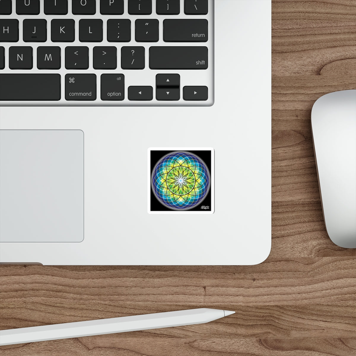 Laptop with a colorful mandala sticker on a wooden desk with a mouse and stylus.