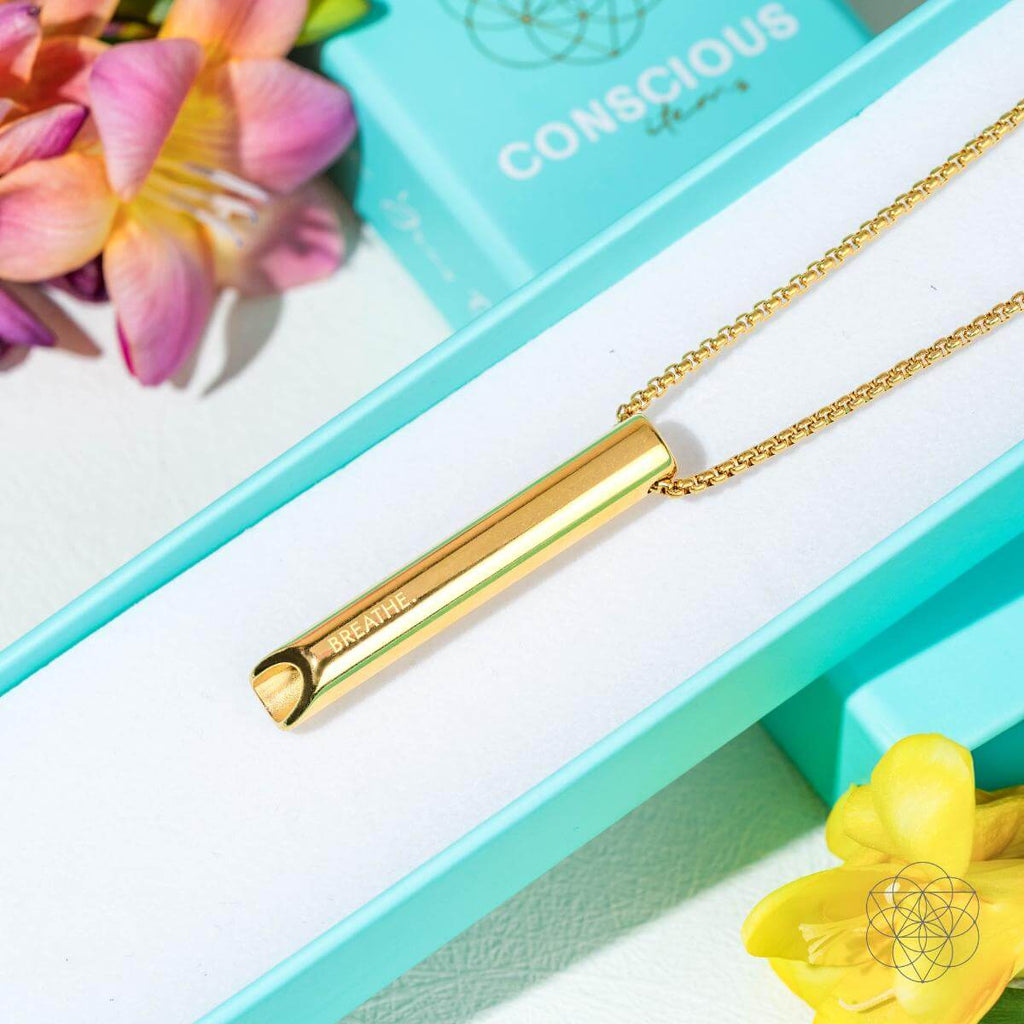Gold necklace with a bar pendant on a turquoise box with flowers around