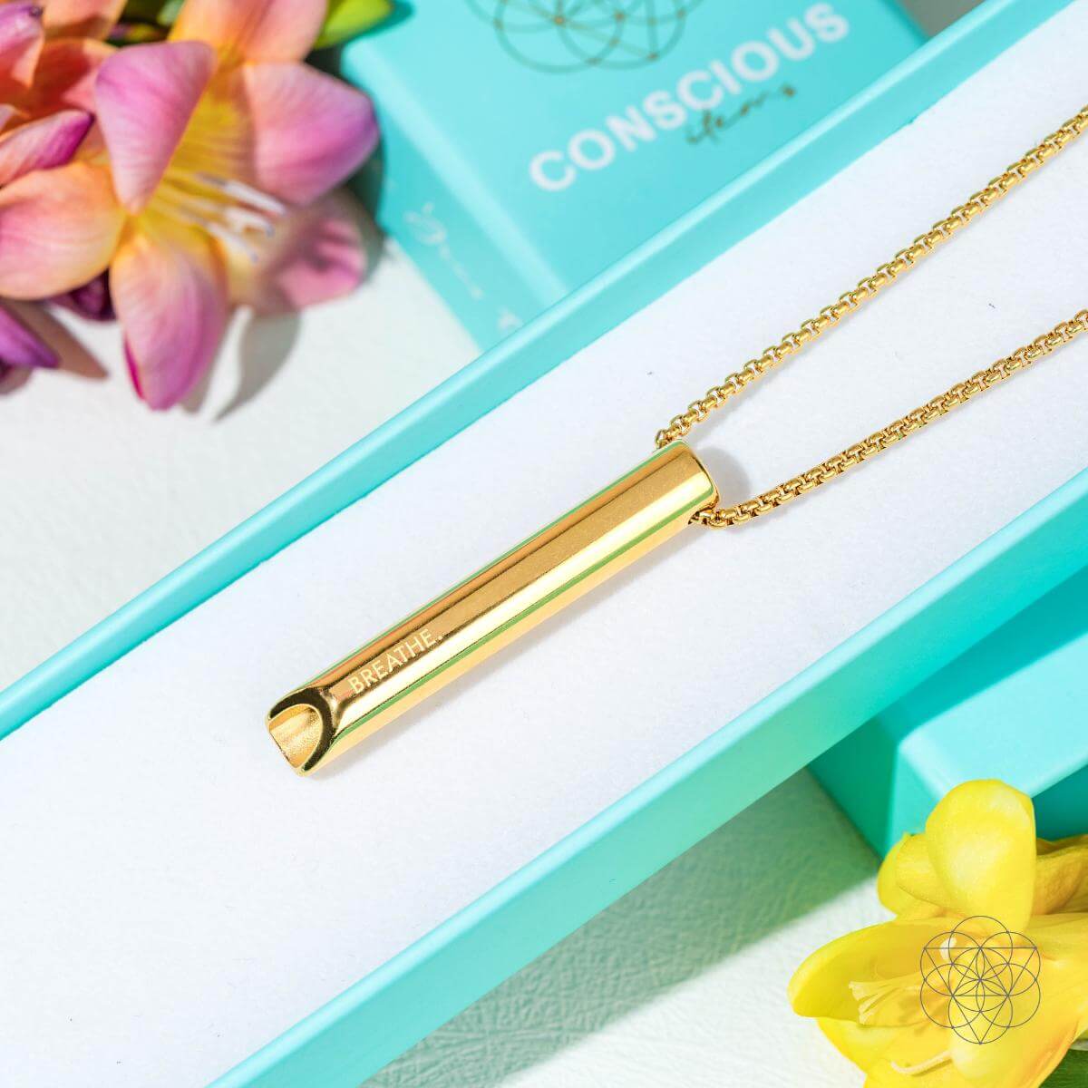 Gold necklace with a bar pendant on a turquoise box with flowers around