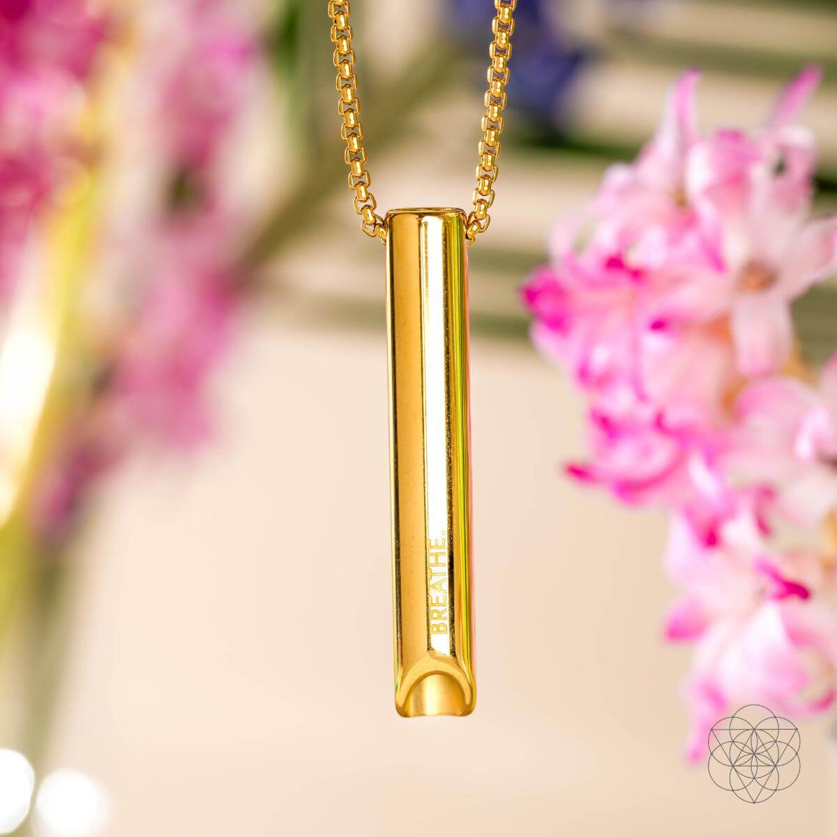 Gold necklace with a cylindrical pendant against a blurred floral background