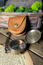 Vintage-style compass with leather case on a rustic wooden surface