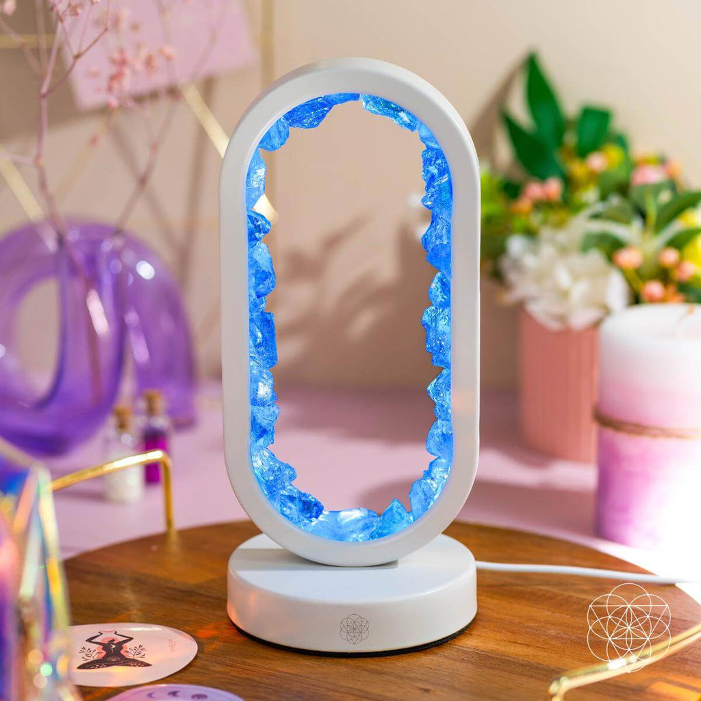 Decorative lamp with blue interior on a wooden surface, blurred background with flowers and decor items.