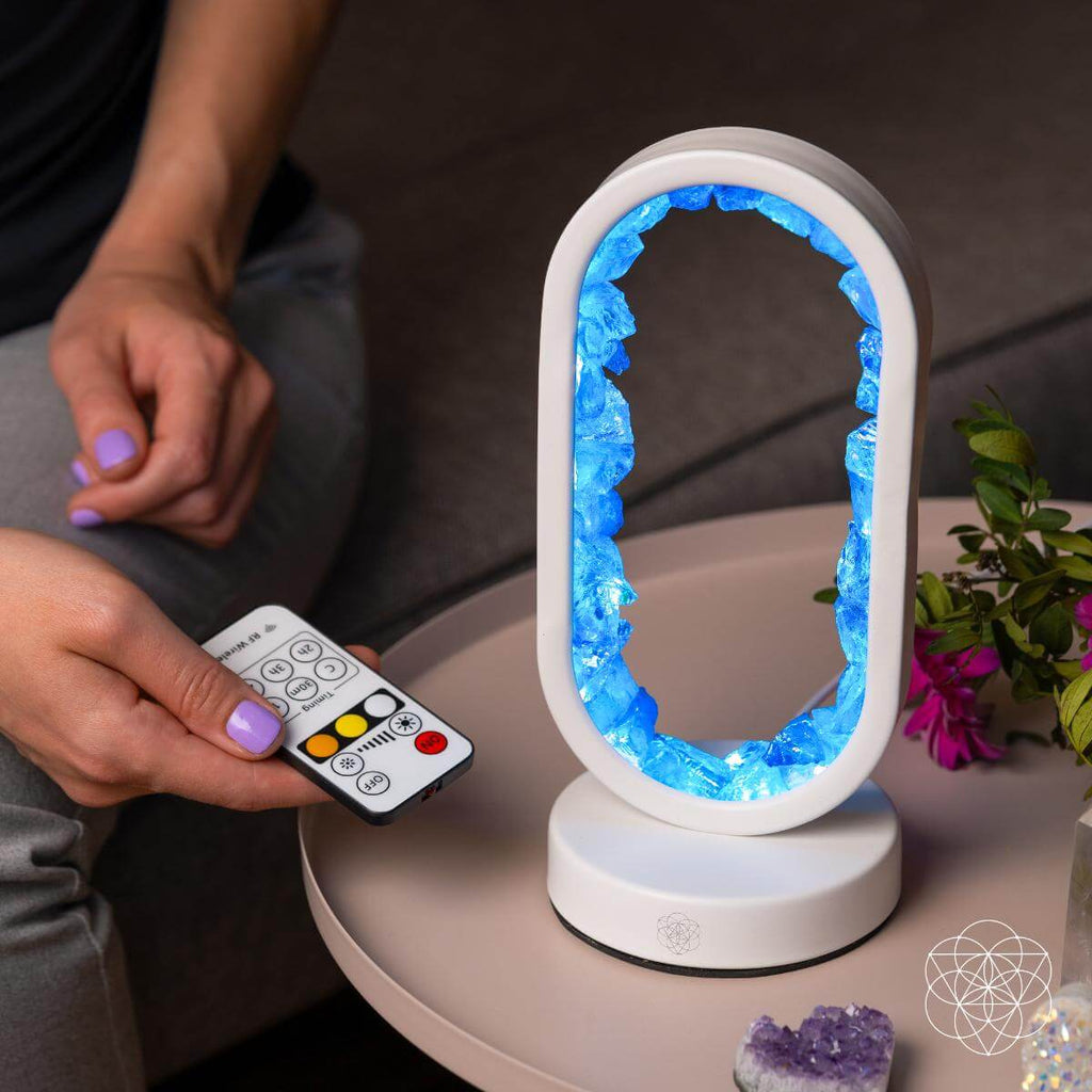 Person holding a remote control next to a glowing crystal-like lamp on a table.