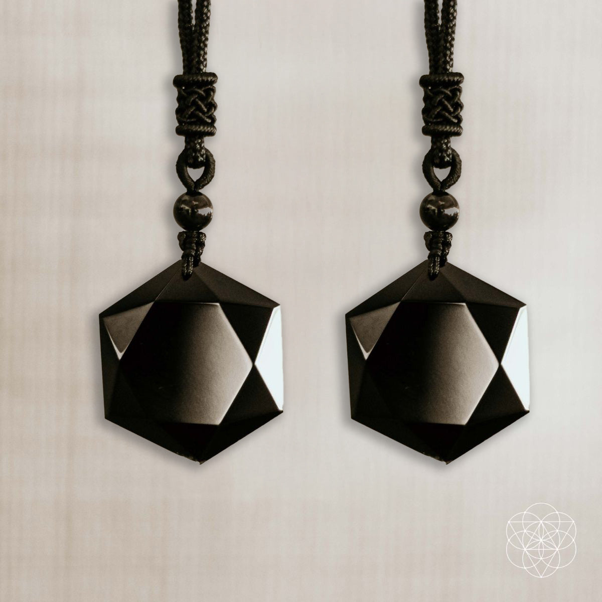 Two black geometric pendant necklaces on a neutral background